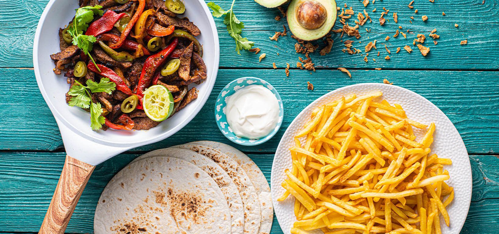 Liellopa fajitas ar sīpolu, papriku, skābo krējumu un plāniem kartupeļiem frī